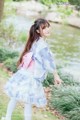 A woman in a blue and pink kimono standing next to a pond.