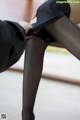 A woman in black stockings and a black skirt is sitting on a bench.