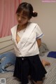 A young girl in a white shirt and black skirt on a bed.