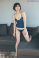 A woman in a blue tank top and panties sitting on a couch.