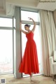 A woman in a red dress standing in front of a window.