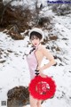 A woman in a pink dress holding a red fan in the snow.