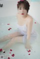 A woman sitting in a bathtub with rose petals on the floor.