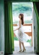 A woman in a white dress standing by a window.