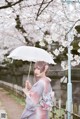 A woman in a kimono holding an umbrella in front of a tree.