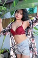 A woman in a red bra top and denim shorts posing for a picture.