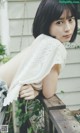 A woman leaning against a wooden fence with her back to the camera.