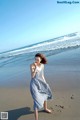 A woman in a blue and white dress walking on the beach.