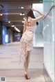 A woman in a pink dress leaning against a glass wall.