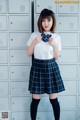 A woman in a school uniform standing in front of lockers.