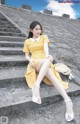 A woman in a yellow dress sitting on some steps.