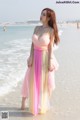 A woman in a pink and yellow dress standing on the beach.