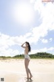 A woman in a white bathing suit standing on a beach.