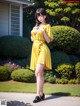 A woman in a yellow dress standing in front of a house.