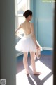 A young ballerina in a white tutu standing in front of a window.