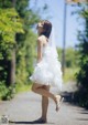 A woman in a white dress is walking down a road.