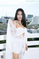 A woman in a white dress posing on a balcony.